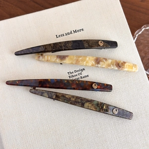 Close-up of minimalist acetate hair clips with gold metal logo on textured book