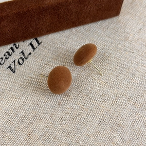 Primo piano dei piccoli orecchini a sfera marroni floccati con perno in metallo oro