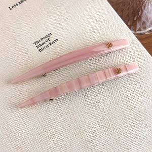 Close-up of pink acetate hair clips with marble texture and golden logo badge detail