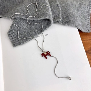 Close-up of silver snake chain with red enamel horse pendant on a grey knit sweater