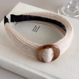 Gros plan du bandeau tricoté beige avec boucle ambre posé sur des livres d'art