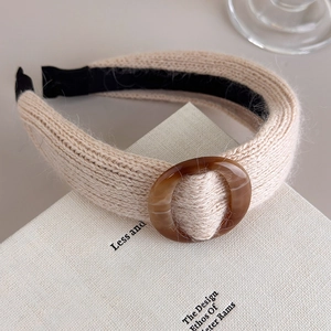 Détail de la maille du bandeau beige avec anneau en résine marbrée sur un livre