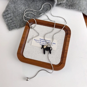 Detail of silver snake chain with black horse pendant and star charm on sweater