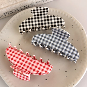 Three acetate checkered hair claws in black, blue, and red displayed on a ceramic tray