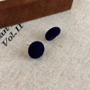 Dettaglio di orecchini a sfera in velluto blu scuro con perni dorati su lino
