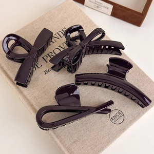 Detailed view of four burgundy bow hair claws on a vintage beige textured linen surface