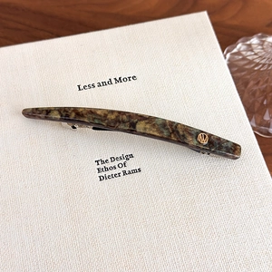 Close-up of marble acetate hair clip with golden logo on a minimalist background