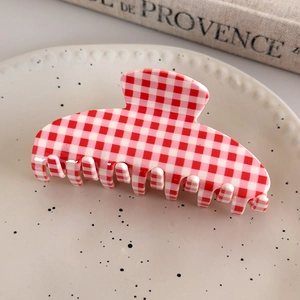 Close-up of a red and white checkered acetate hair claw clip on a ceramic tray