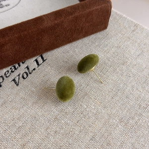 Dettaglio macro di orecchini a lobo floccati verde oliva su sfondo in tessuto di lino beige