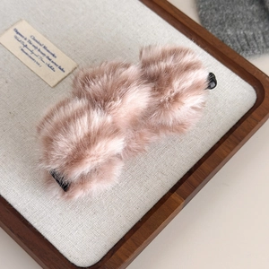 Détail d'une barrette banane en peluche rose poudré sur un plateau en bois épuré
