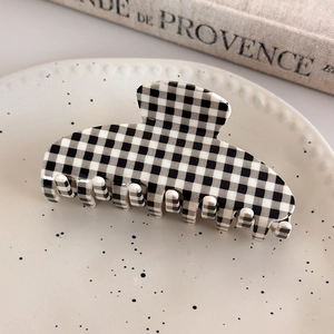 Close-up of a large black and white checkered hair claw clip on a ceramic tray