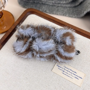 Vue détaillée de la pince banane en peluche avec pompons doux bleus et marrons