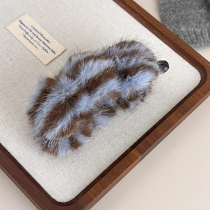 Détail d'une pince banane en fausse fourrure rayée marron et bleu sur plateau en bois
