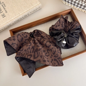 Detailed macro view of leopard print fabric scrunchie with gold metal charm in a wooden tray