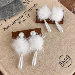 Elegante weiße Pelz-Pompon-Ohrringe mit Perlen auf einem Vintage-Buchhintergrund
