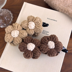 Detailed close-up of knitted yarn flower hair clips in brown and beige tones on a book