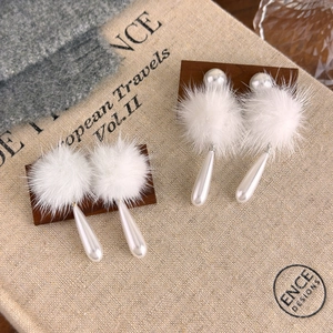 Elegante weiße Pelz-Pompon-Ohrringe mit Tropfenperlen auf einem dunklen Holzständer