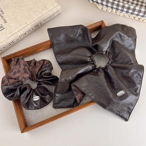Detail view of coffee leopard print scrunchie and leather bow on a rustic wooden tray