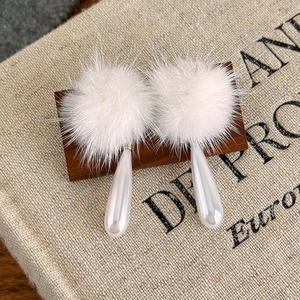 Detailansicht langer Tropfenohrringe mit weißen flauschigen Pelzpompons und Perlenanhängern