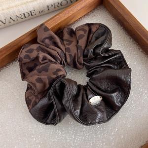 Detail of leopard print fabric and dark brown faux leather scrunchie with metal charm
