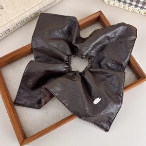 Detail of dark brown leather texture hair scrunchie with a stylish oval metal tag