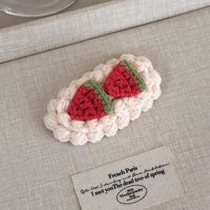 Detailed view of handmade crochet watermelon hair clip with pink wavy base on linen fabric