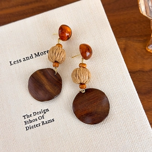 Detail showing retro wood earrings with amber resin and woven raffia beads on a book