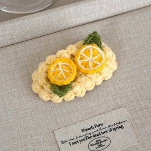 Detail of handmade crochet hair clip featuring lemon slices on a yellow woven base