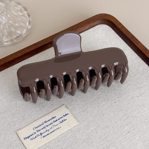 Détail d'une grande pince à cheveux marron foncé sur tissu en lin et plateau en bois