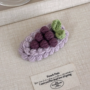 Detail view of handmade crochet grape hair clip with purple yarn on a beige linen tray