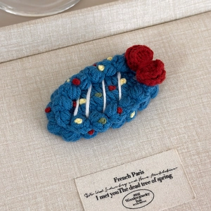 Close-up of royal blue hand-crocheted fruit hair clip with red flowers on fabric