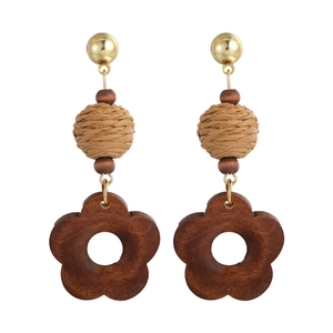 Detailed macro view of woven raffia ball and dark brown wooden flower drop earrings