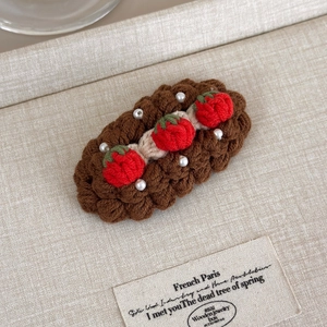 Detail of handmade crochet hair clip featuring red strawberries and white pearls texture