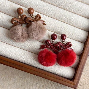 Détail de boucles d'oreilles rétro à nœud et pompon en marron et rouge pour l'automne