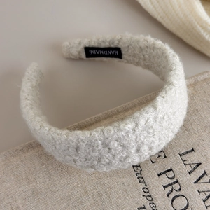 Detail of cream sherpa headband with black handmade label on soft linen texture