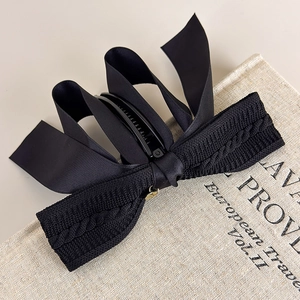 Detail of black knitted bow banana clip with golden pendant on a vintage book