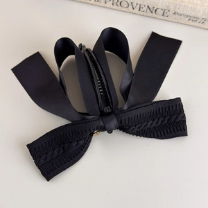 Detailed close-up of a black bow banana clip with elegant knit and satin textures
