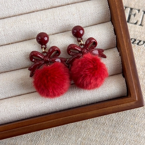 Détail des boucles d'oreilles avec nœud en velours et pompon dans un écrin à bijoux
