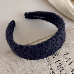 Close-up of black curly plush headband with handmade label on vintage linen book