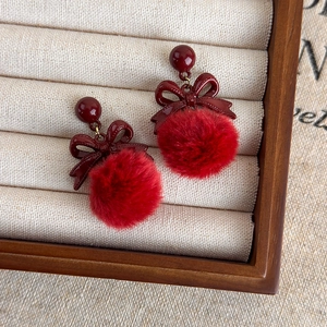 Détail de boucles d'oreilles pompon rouge avec nœud en métal sur boîte à bijoux