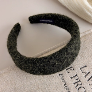 Detail of dark green textured fleece headband with handmade label on linen surface