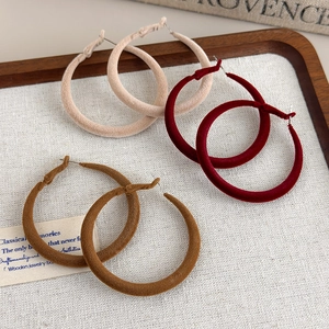 Detail of three pairs of large C-shaped velvet earrings in beige, wine red, and brown colors
