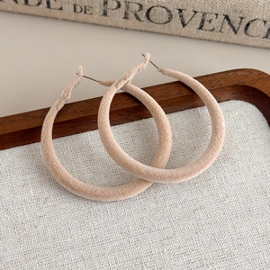 Close-up of elegant beige flocked hoop earrings on a natural wooden and linen background