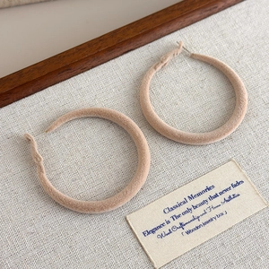 Close-up of winter velvet hoop earrings in nude pink flocking texture on a beige fabric