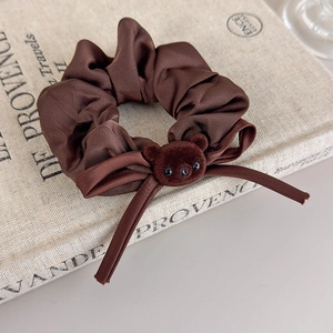 Detail of dark brown satin scrunchie with a cute flocked bear head charm on vintage book