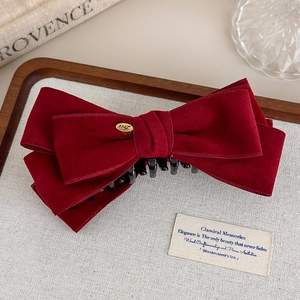 Close-up of a burgundy velvet bow hair clip with a gold metal 'Love' tag in a tray