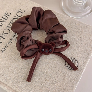 Detail of coffee brown satin scrunchie with a velvet bear charm and elegant ribbon bow