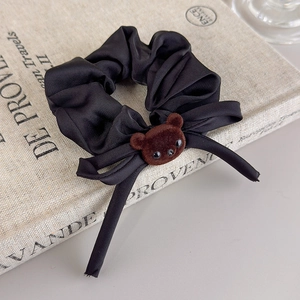 Detail of a black satin scrunchie featuring a cute brown flocked bear charm on a book