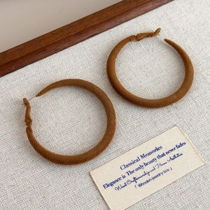 Detailed view of large brown velvet flocking hoop earring on textured fabric backdrop