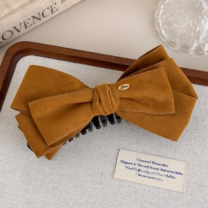 Detailed close-up of brown suede bow hair clip with gold Love emblem and strong plastic claw